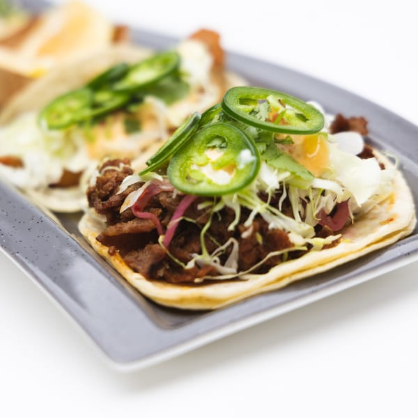 Two Korean beef tacos with shredded cabbage, pickled onions, and sliced jalapeños on a gray plate.