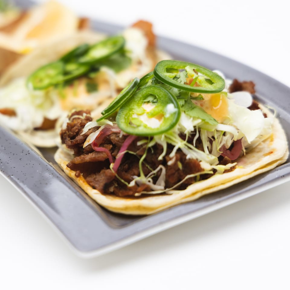 Two Korean beef tacos with shredded cabbage, pickled onions, and sliced jalapeños on a gray plate.