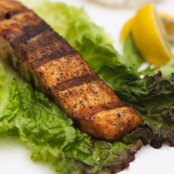 Grilled salmon fillet with grill marks, served on fresh green lettuce with a lemon wedge.
