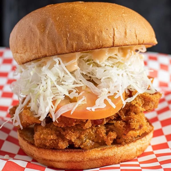 Crispy fried chicken sandwich with shredded cabbage, tomato, and sauce on a bun.