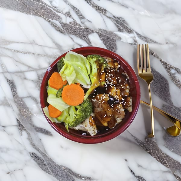A red bowl of Korean teriyaki chicken, rice, broccoli, cabbage, and carrots on a marble surface.