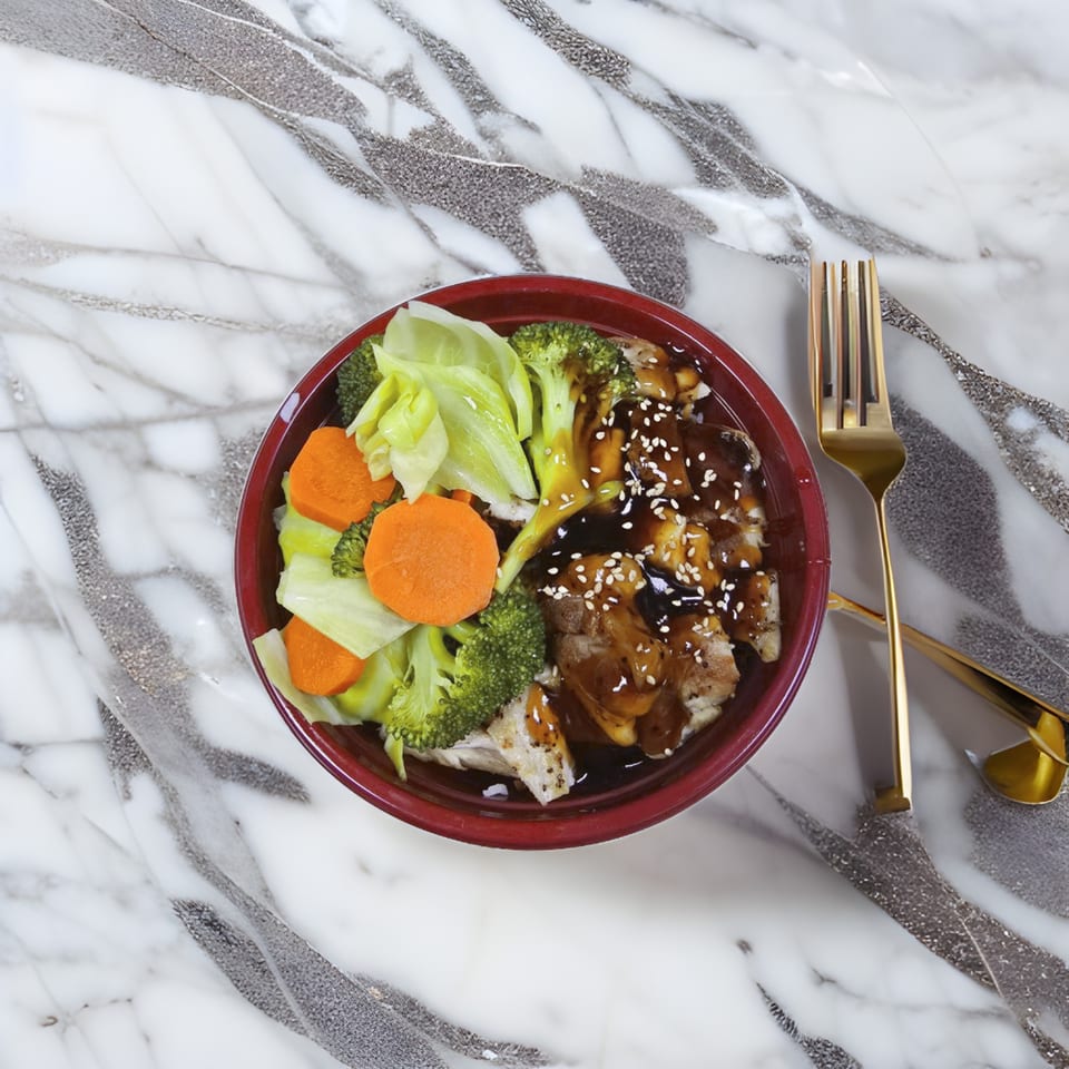 A red bowl of Korean teriyaki chicken, rice, broccoli, cabbage, and carrots on a marble surface.