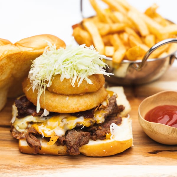 A Korean bulgogi sandwich with onion rings and shredded cabbage, served with fries and ketchup.
