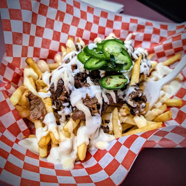 Korean bulgogi fries with white sauce and sliced jalapeños in a red and white checkered basket.